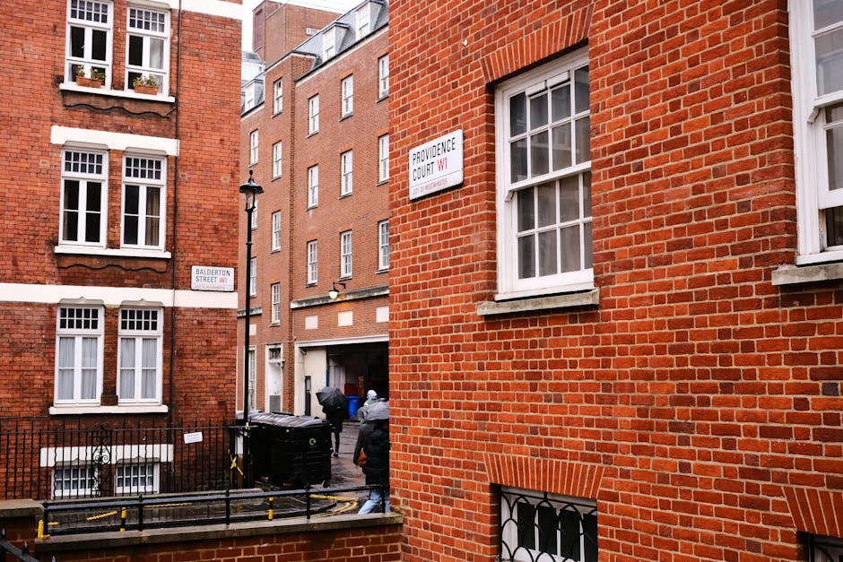 The image depicts an indoor area, possibly a storage or loading bay, with a white double door set into a brick wall. In front of the door, there are two stacks of black plastic crates or containers, s